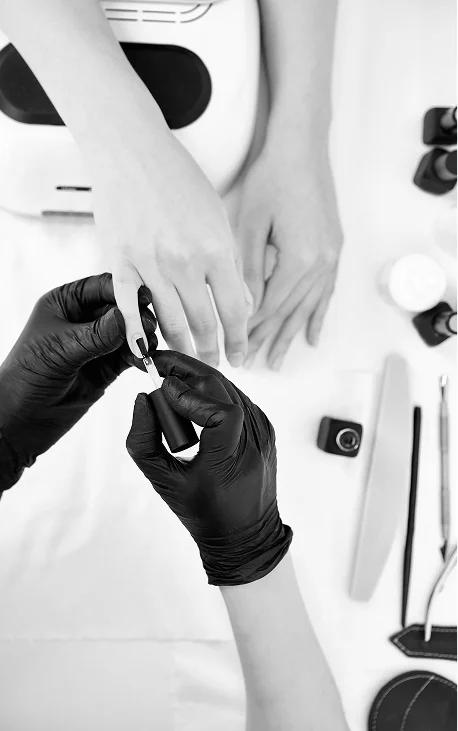 Een nagelstyliste met zwarte handschoenen brengt gel-lak aan op de nagels van de klant.